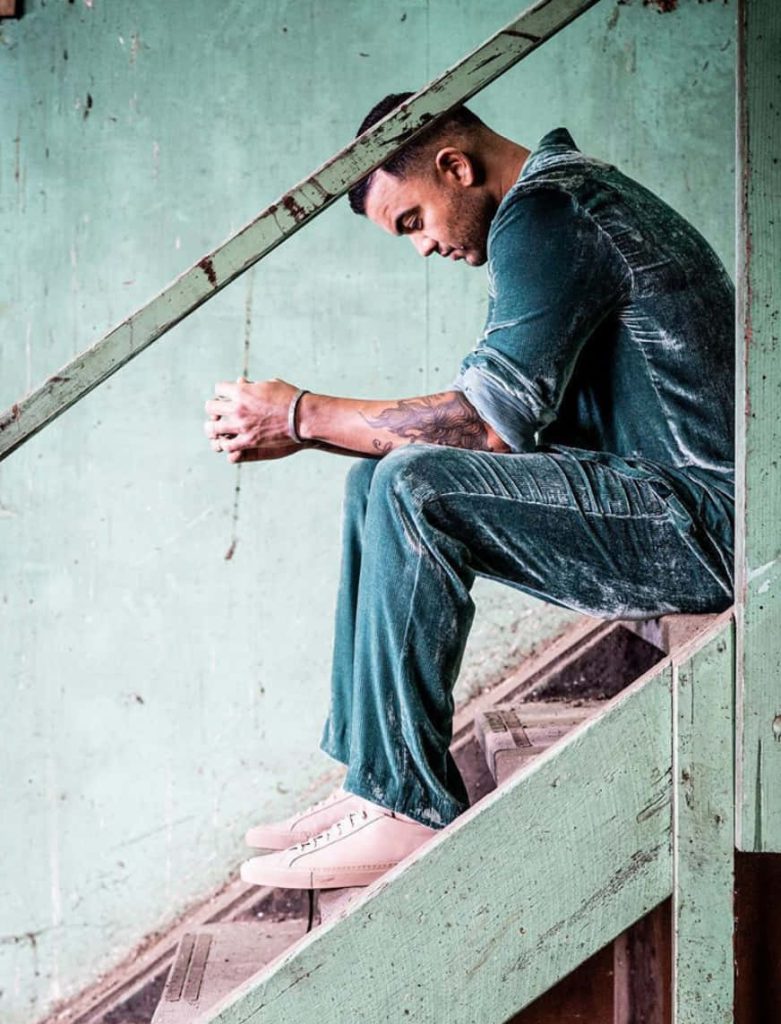 Guy Sebastian in teal velvet suit seated on rustic stairs with moody lighting background wallpaper