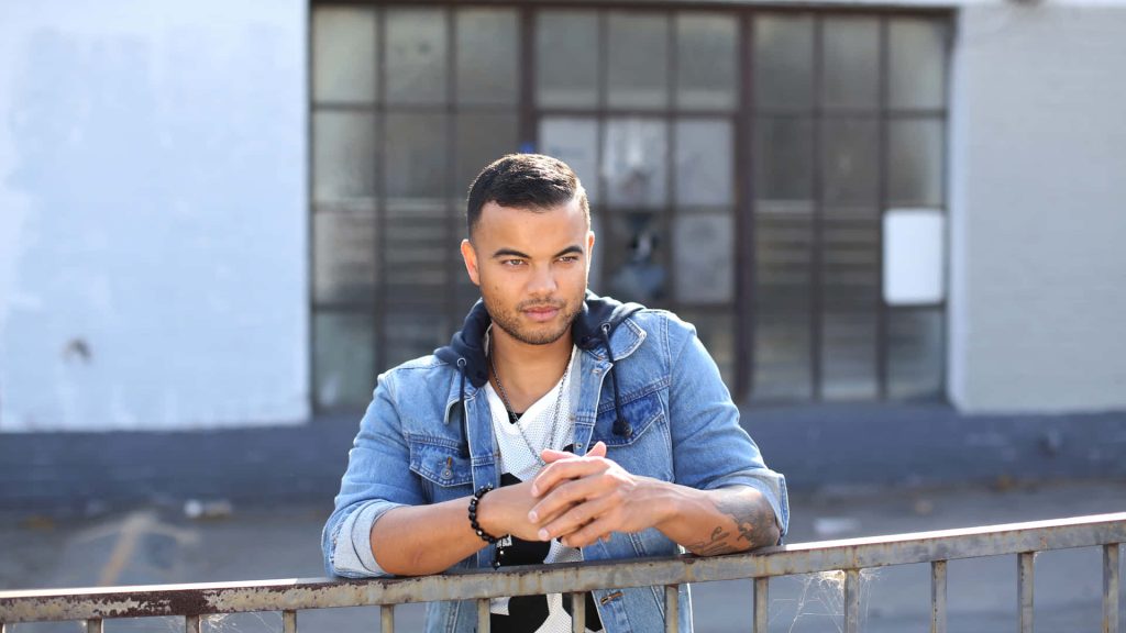 Australian singer Guy Sebastian in denim jacket poses thoughtfully by metal railing urban style Wallpaper