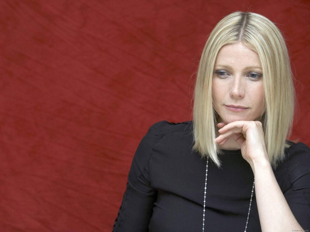 Gwyneth Paltrow portrait thoughtful pose blonde bob black outfit deep red textured wallpaper