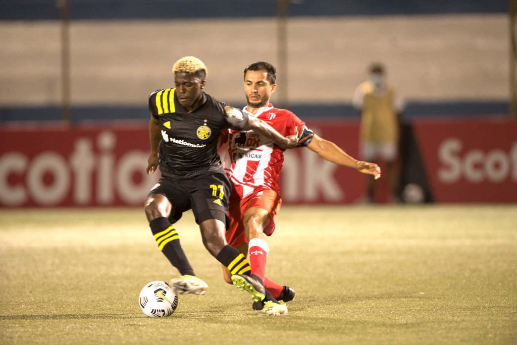 Columbus Crew forward Gyasi Zardes challenges Real Estelí defender in intense soccer match under stadium lights Wallpaper