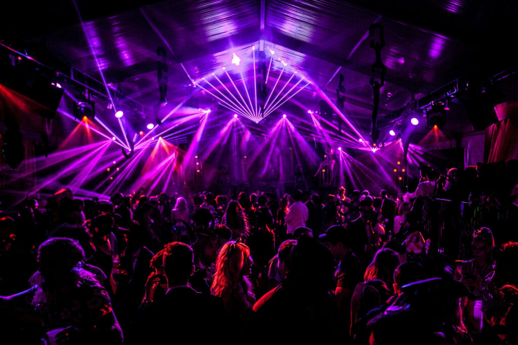 Vibrant nightclub crowd dancing under purple laser lights in a lively party tent at night Wallpaper