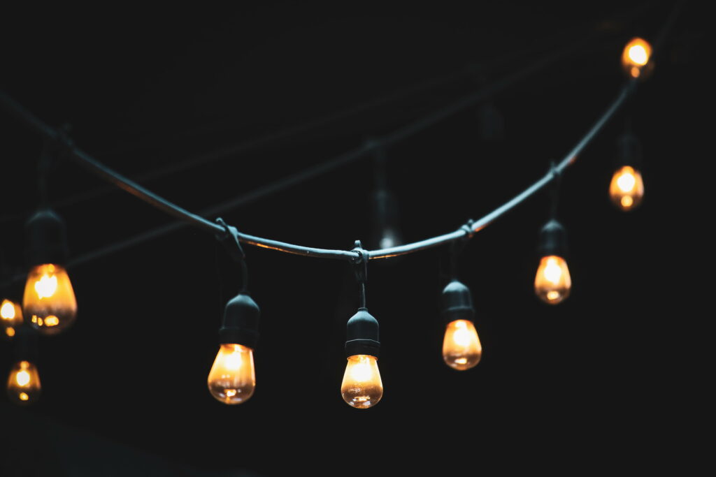 Warm glowing incandescent string lights on dark wire against black backdrop wallpaper background