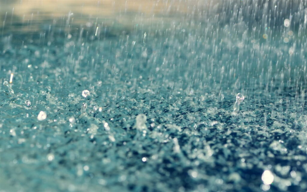 Close-up of raindrops splashing on blue water surface with ripples and sparkling reflections Wallpaper