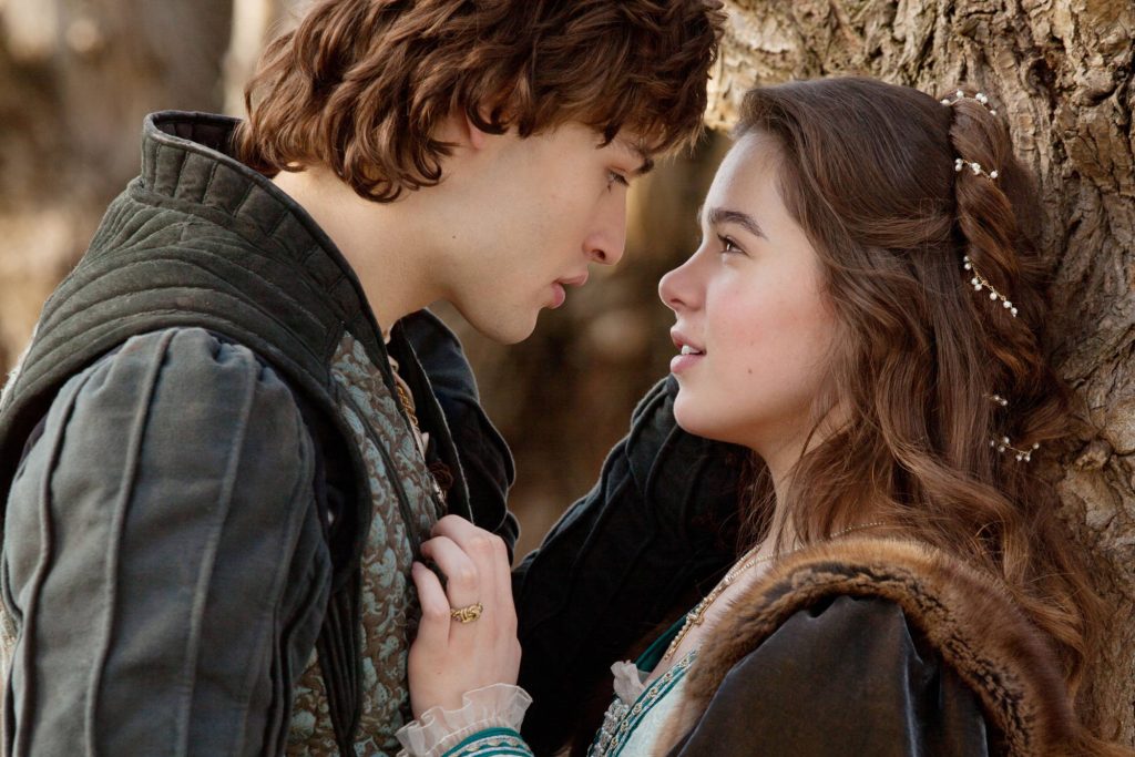 Hailee Steinfeld and Douglas Booth in Romeo and Juliet period costumes sharing a tender gaze Wallpaper