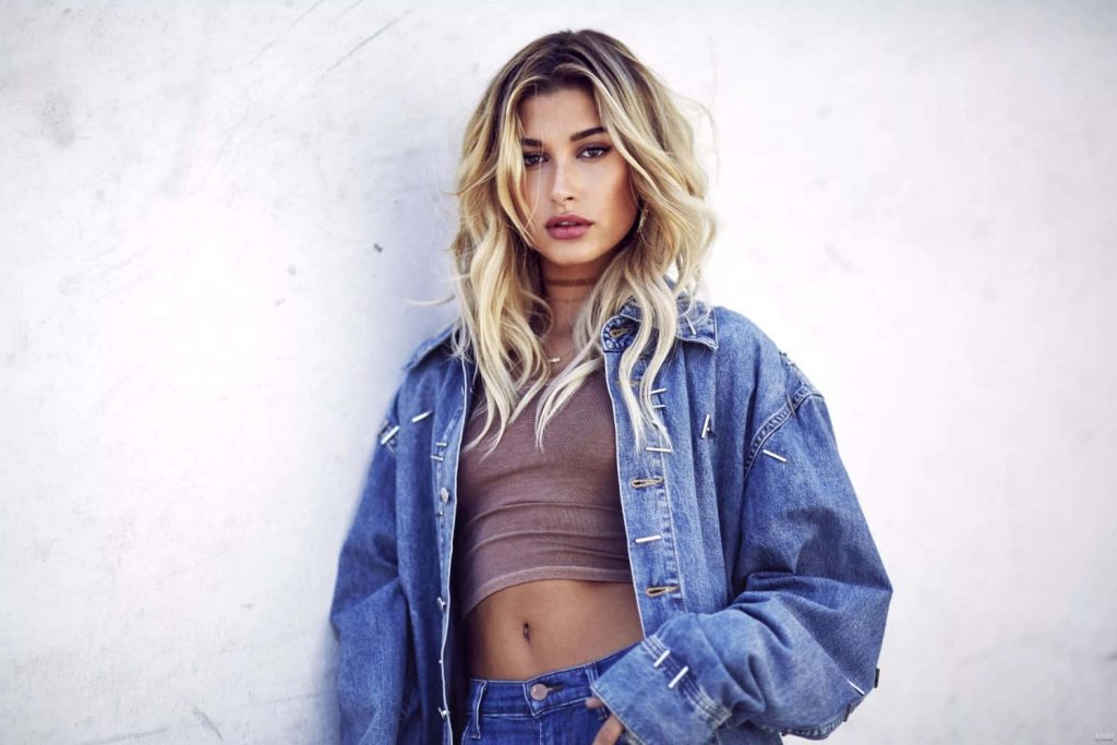 Hailey Bieber fashion portrait in oversized denim jacket and brown crop top on white wall Wallpaper