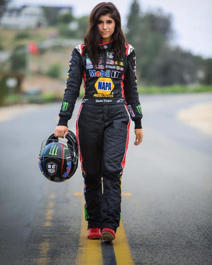 Hailie Deegan confident race car driver walking on asphalt track in black red white racing suit Wallpaper