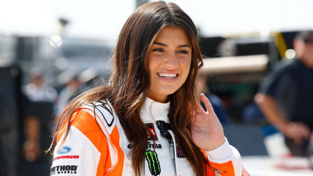 Hailie Deegan in white orange Ford Performance racing suit smiling bright at race track wallpaper