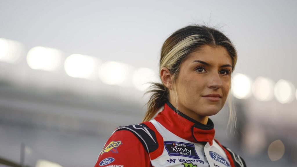NASCAR driver Hailie Deegan in Ford racing suit with blurred stadium background wallpaper