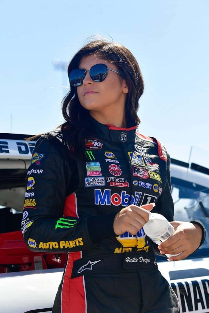 Race car driver Hailie Deegan in black red racing suit sunglasses holding water bottle outdoors Wallpaper