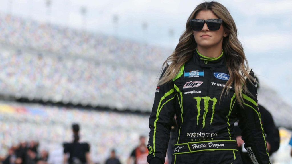 Hailie Deegan in Monster Energy racing suit walking confidently by racetrack crowd wallpaper