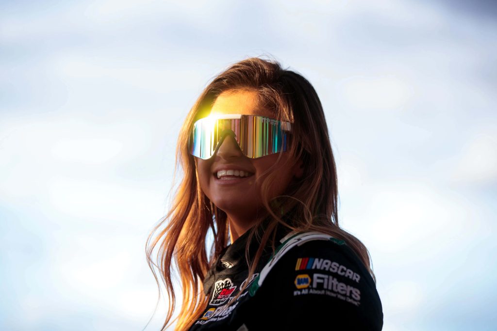 NASCAR driver Hailie Deegan smiling in black racing gear with reflective sunglasses outdoors Wallpaper