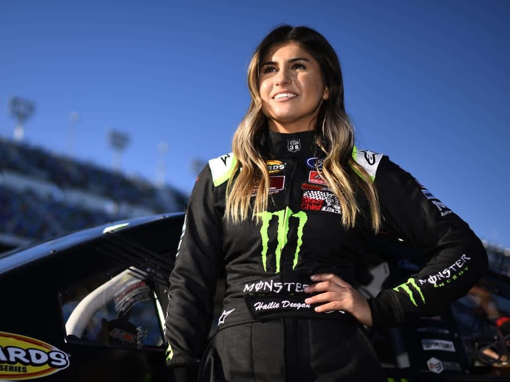 NASCAR driver Hailie Deegan in Monster Energy suit posing trackside under blue sky wallpaper