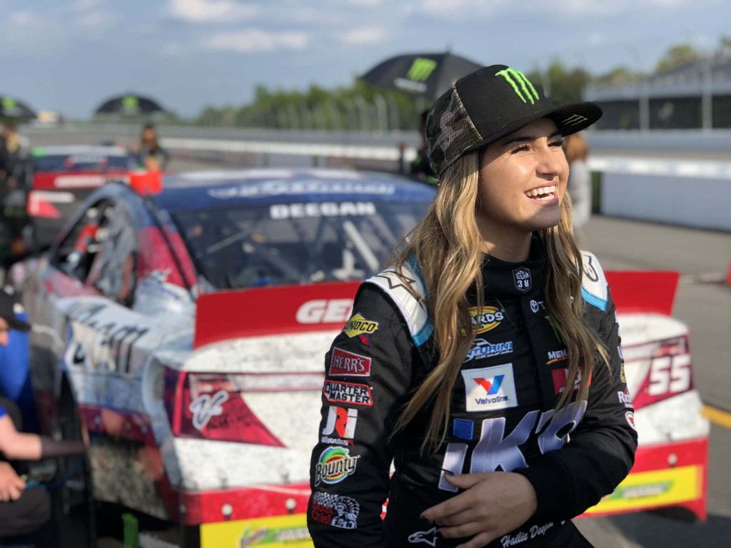 Race car driver Hailie Deegan in black suit and Monster Energy cap by car 55 outdoors Wallpaper