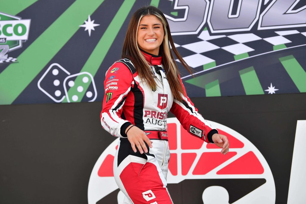Hailie Deegan in red white black racing suit with dynamic checkered motorsports background wallpaper