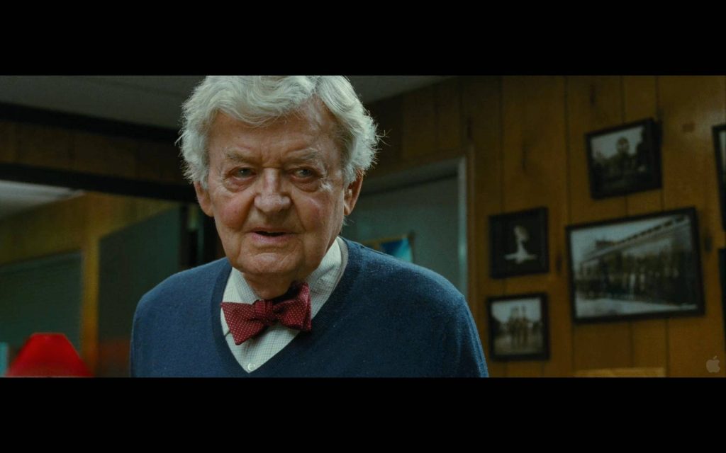 Hal Holbrook in blue sweater and maroon bow tie against rustic wood wall with vintage photos Wallpaper