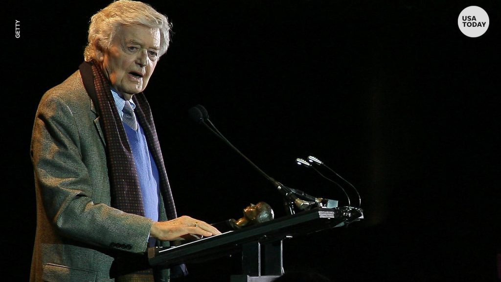 Hal Holbrook on stage speaking behind podium spotlighted with award and dark background wallpaper