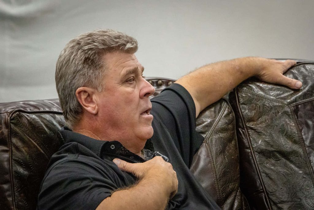 Professional golfer Hal Sutton in black polo shirt relaxing on brown leather couch in natural light Wallpaper