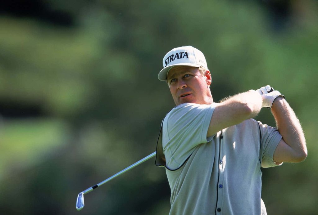 Golf legend Hal Sutton in iconic Strata cap powering a swing against lush green background Wallpaper