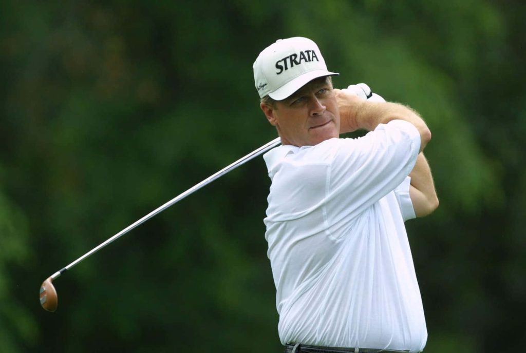 Professional golfer Hal Sutton mid-swing wearing white polo and Strata cap on green golf course Wallpaper