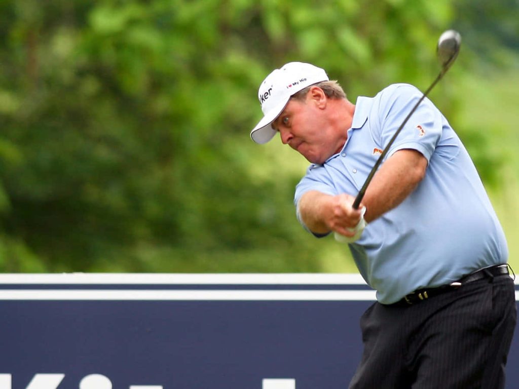 Professional golfer Hal Sutton mid swing on lush green golf course in light blue polo and white cap Wallpaper