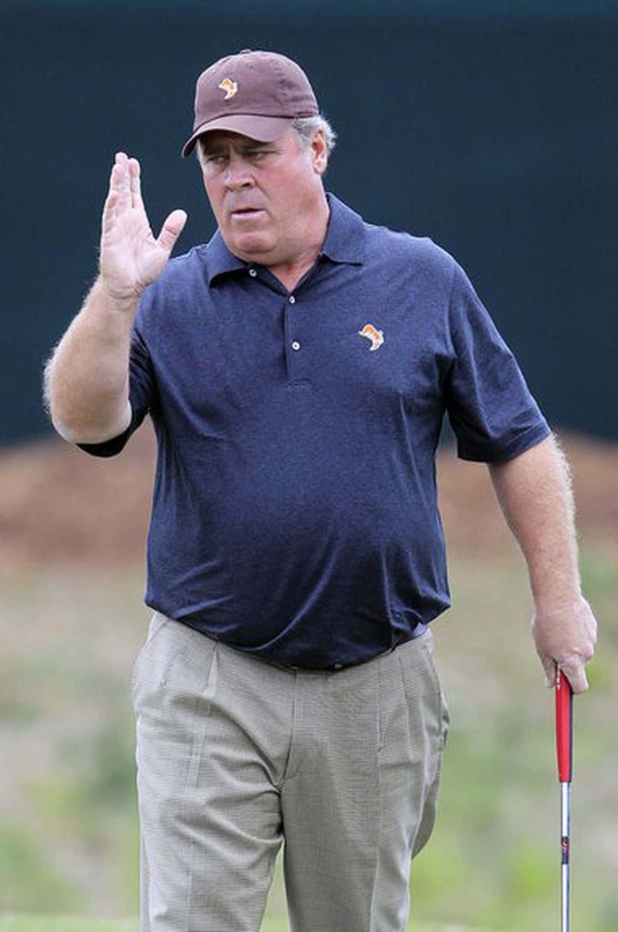 Professional golfer Hal Sutton walking on golf course holding club wearing navy polo and brown cap Wallpaper