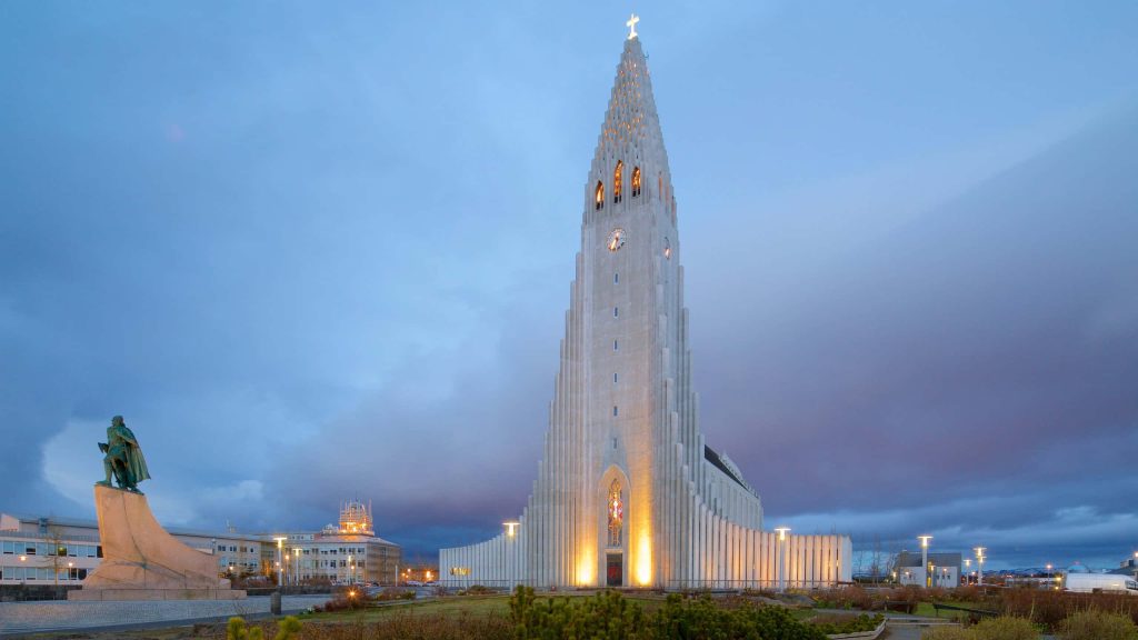 Hallgrímskirkja church in Reykjavík glowing at twilight with Leif Erikson statue foreground blue sky Wallpaper