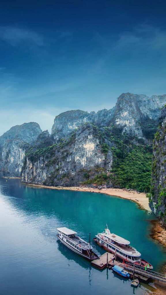 Scenic Halong Bay Vietnam with ships docked turquoise waters limestone cliffs and lush greenery Wallpaper
