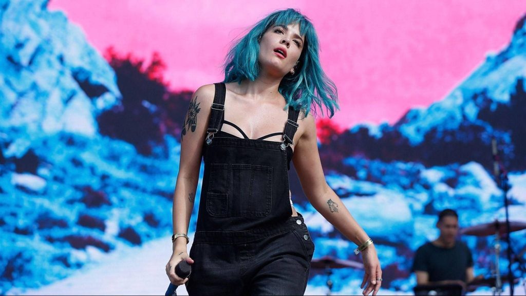 Halsey live performance with blue bob and black overalls on vibrant abstract digital stage background Wallpaper