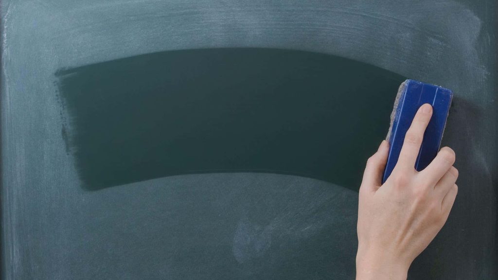 Hand erasing green blackboard with blue eraser creating clean educational workspace background Wallpaper