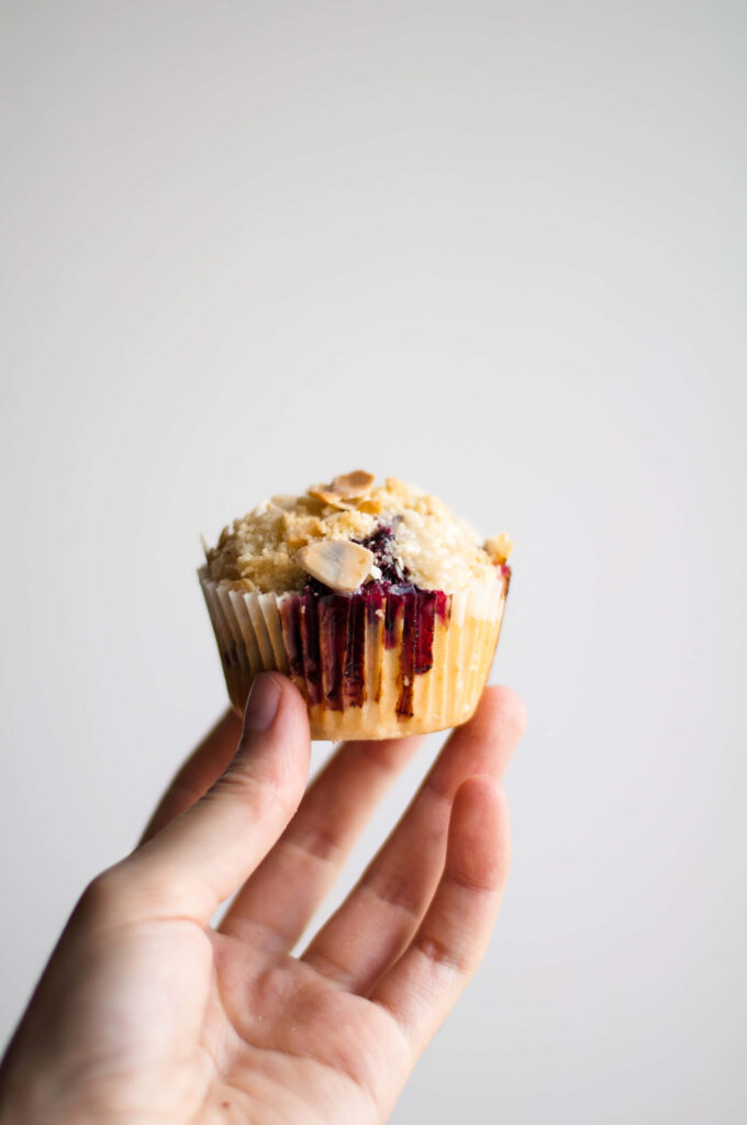 Hand holding homemade cupcake with berry sauce swirl and crumbled topping on white background Wallpaper