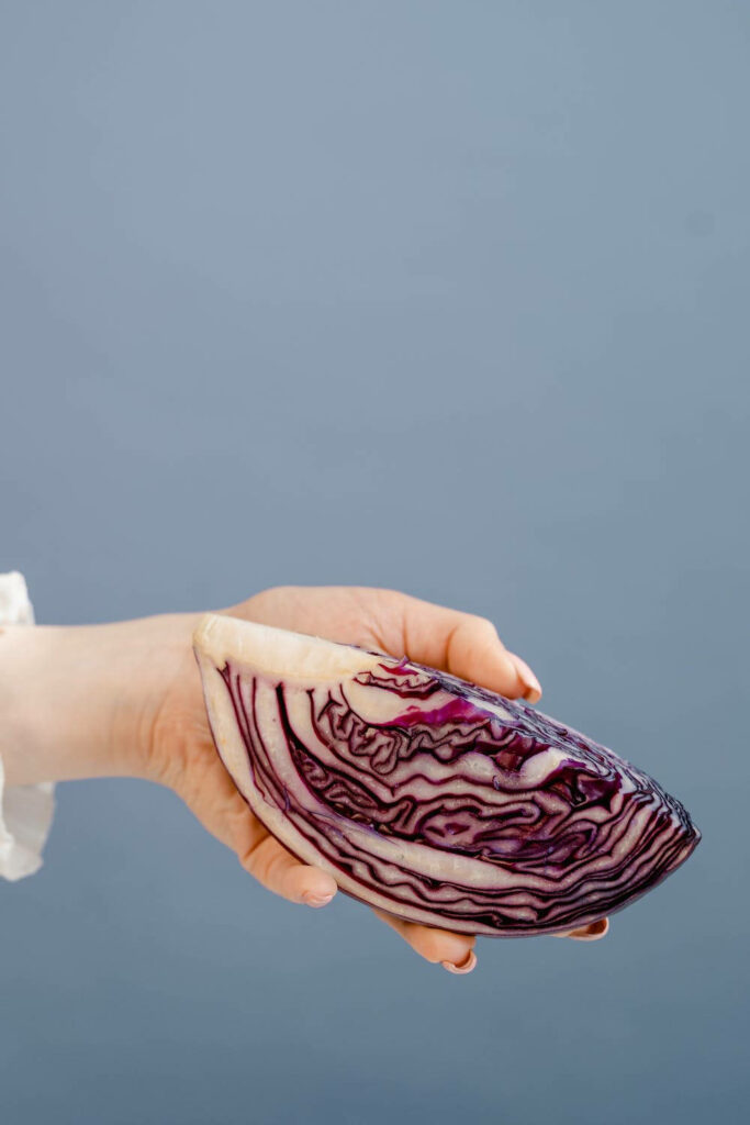 Hand holding freshly sliced purple cabbage showing vibrant swirling patterns on blue background Wallpaper