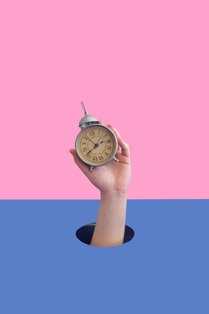 Hand holding vintage clock against vibrant pink and blue background symbolizing time concept Wallpaper