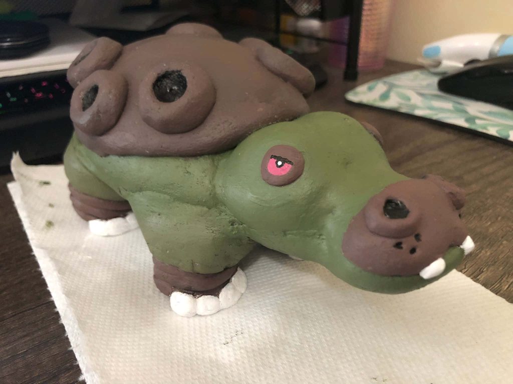 Handmade clay Hippowdon figure with brown back green body and red eyes on desk background Wallpaper