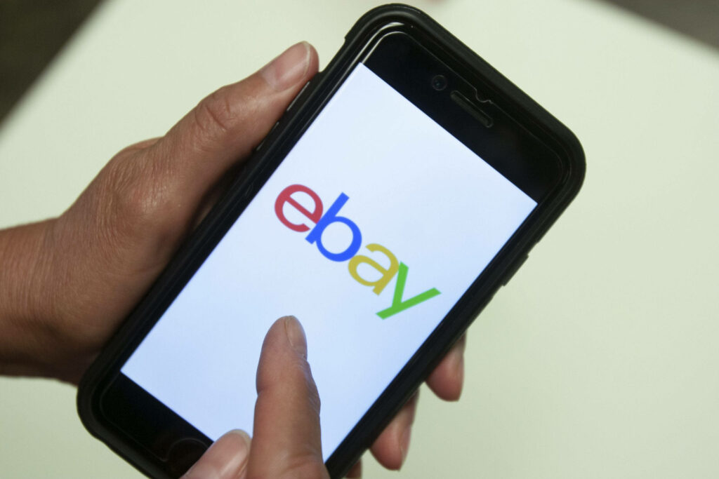 Hands holding smartphone showcasing colorful eBay logo symbolizing e-commerce technology background Wallpaper