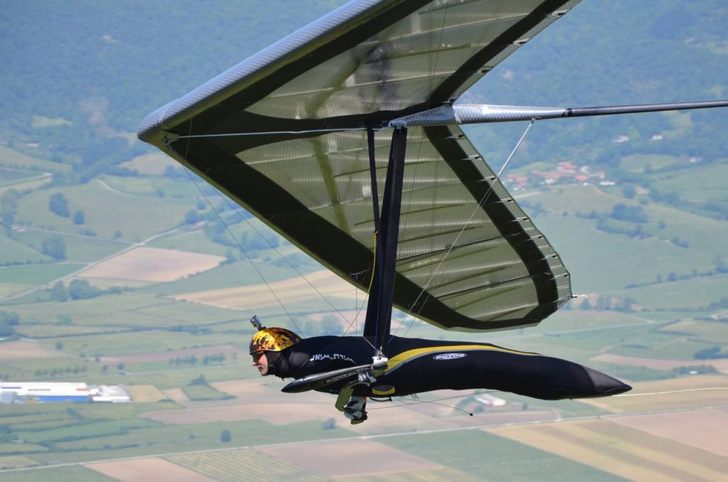 Hang glider soaring over green fields with pilot wearing helmet GoPro in bright natural light Wallpaper