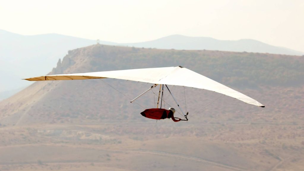 Pilot in red harness hang gliding over desert landscape soaring high freedom adventure sport Wallpaper