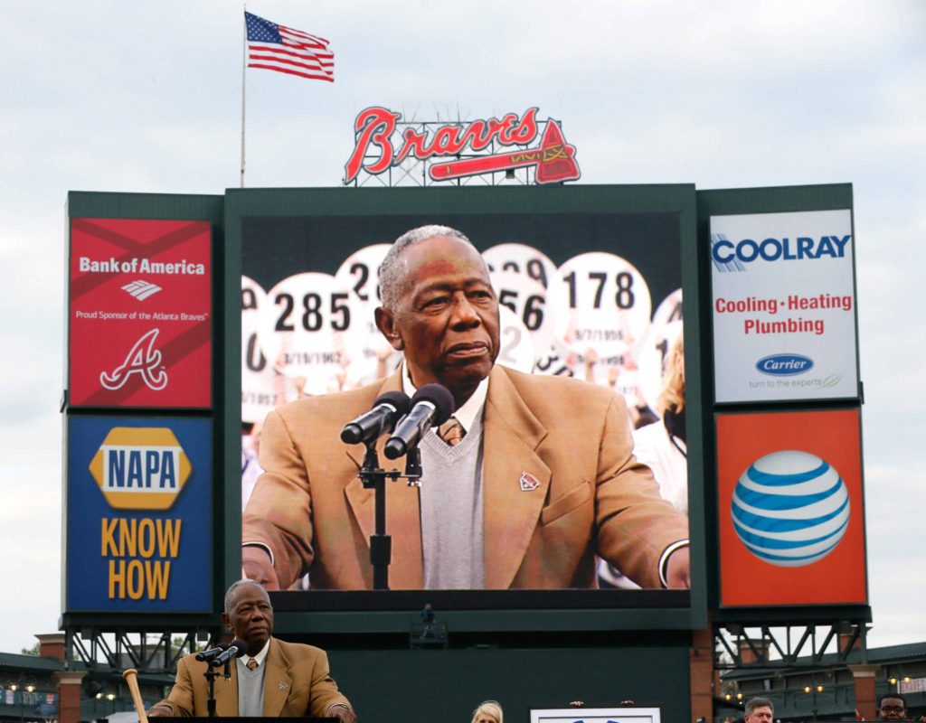 Hank Aaron speaking at Atlanta Braves stadium ceremony with scoreboard and American flag background Wallpaper