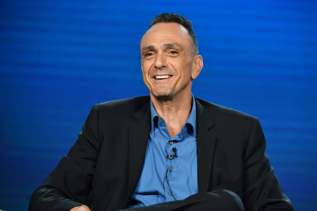 Hank Azaria portrait in black blazer and blue shirt against vibrant blue studio background wallpaper