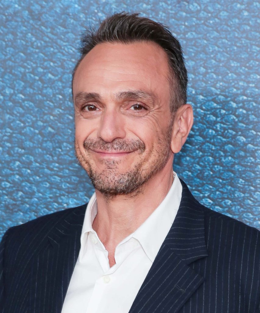 Portrait of actor Hank Azaria smiling in dark pinstriped suit with blue textured background Wallpaper