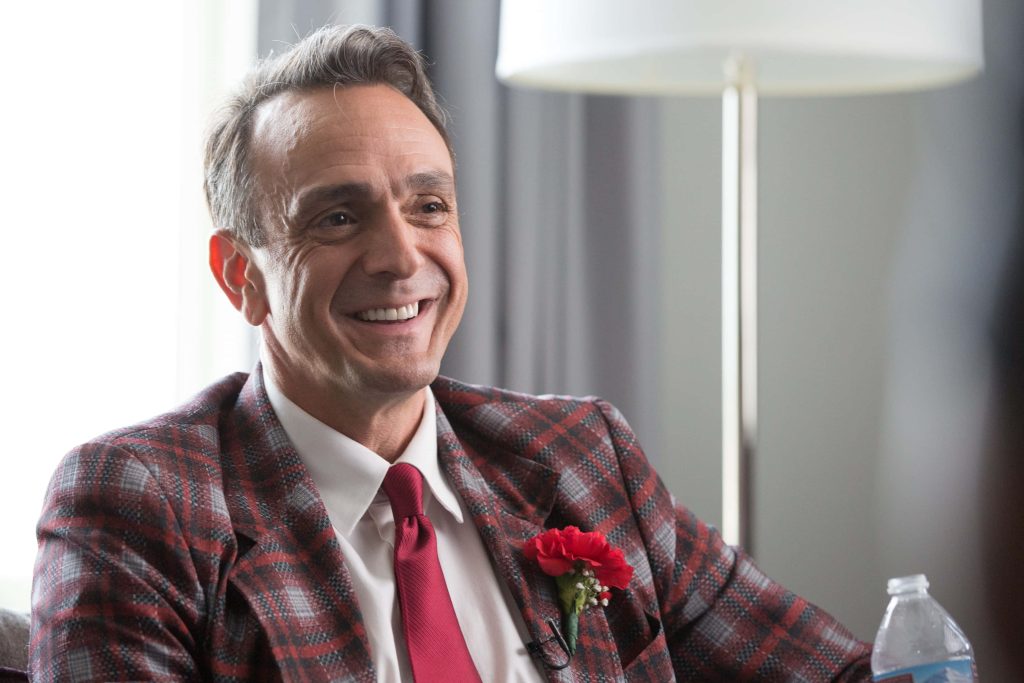 Hank Azaria smiling in red plaid blazer white shirt red tie boutonniere professional portrait wallpaper