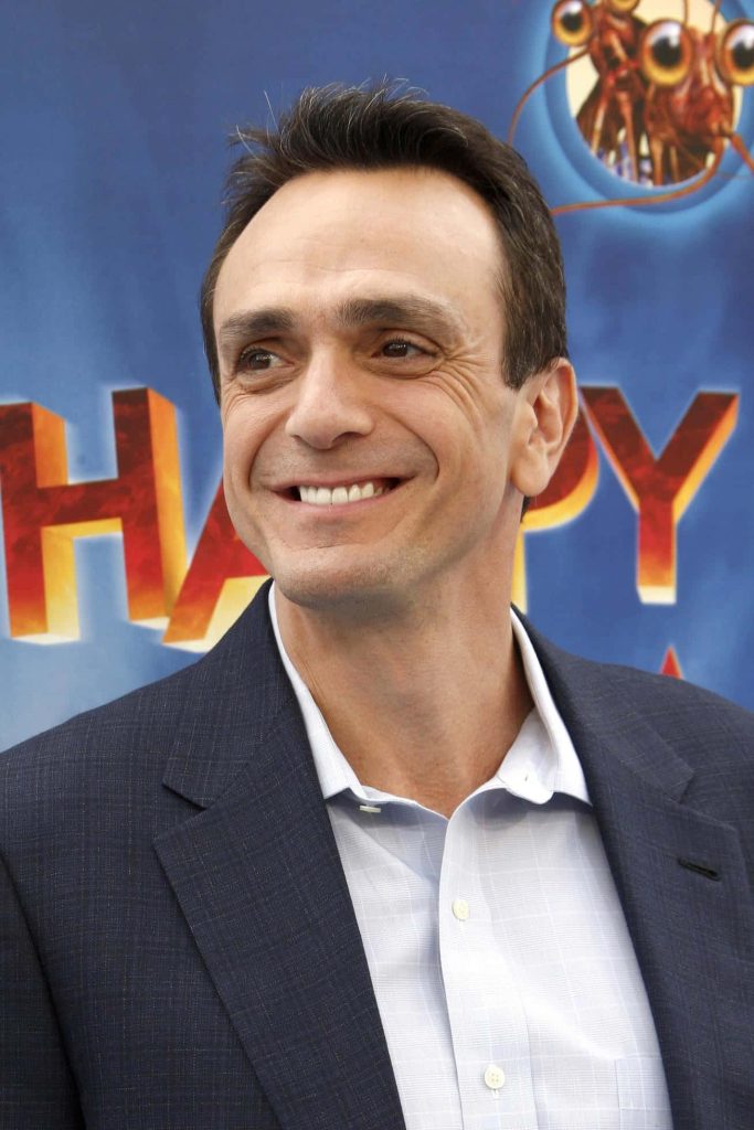 Hank Azaria smiling in navy blazer at Happy Feet Two premiere with vibrant blue background Wallpaper