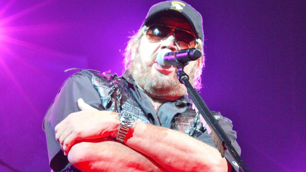 Hank Williams Jr performing live in signature cap sunglasses vest purple stage lights wallpaper