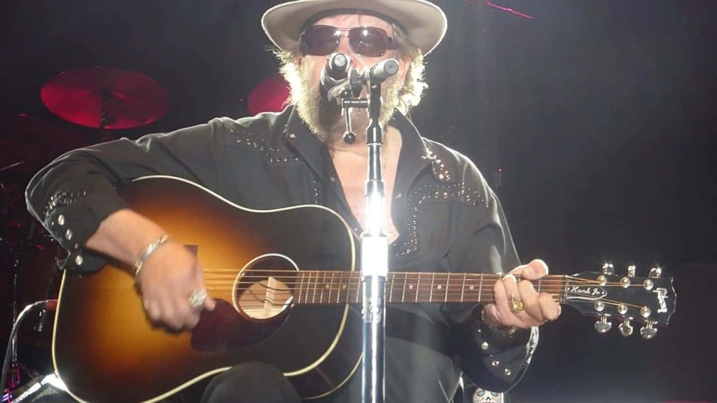 Hank Williams Jr on stage with sunburst Gibson guitar wearing hat and sunglasses country music wallpaper