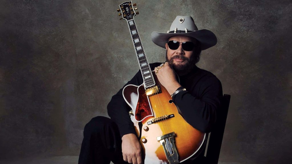 Hank Williams Jr in cowboy hat and sunglasses with guitar moody textured studio portrait wallpaper