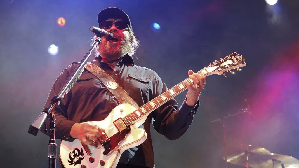 Hank Williams Jr. live performance playing white electric guitar in vibrant concert lighting Wallpaper