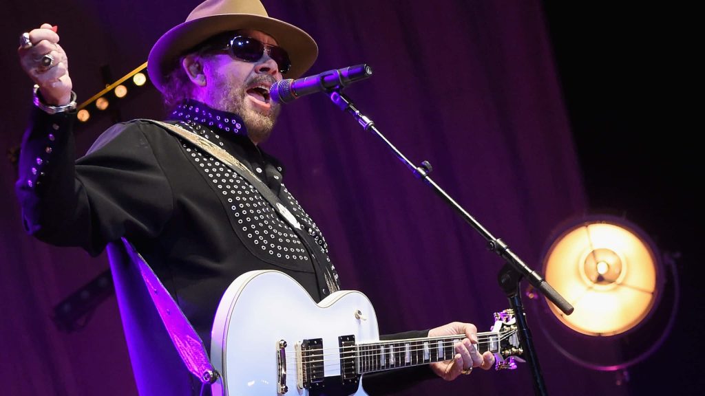 Hank Williams Jr playing white electric guitar in studded black shirt on purple stage spotlight Wallpaper