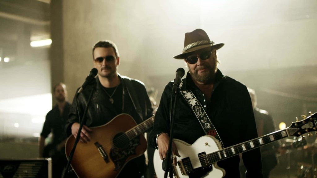 Hank Williams Jr and Eric Church country music performance with guitars on dim hazy stage wallpaper