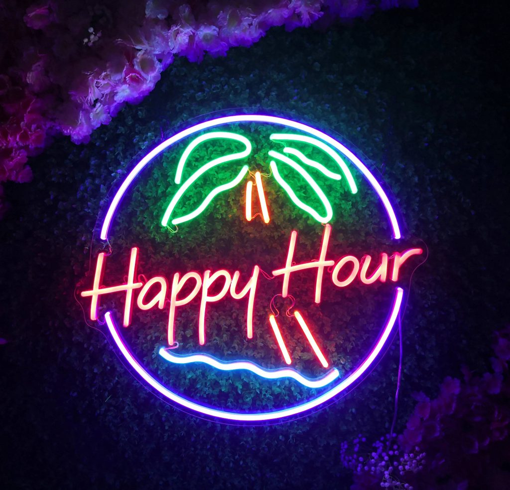Happy Hour neon sign with palm tree on purple circle against dark hedge wall with pink flowers Wallpaper