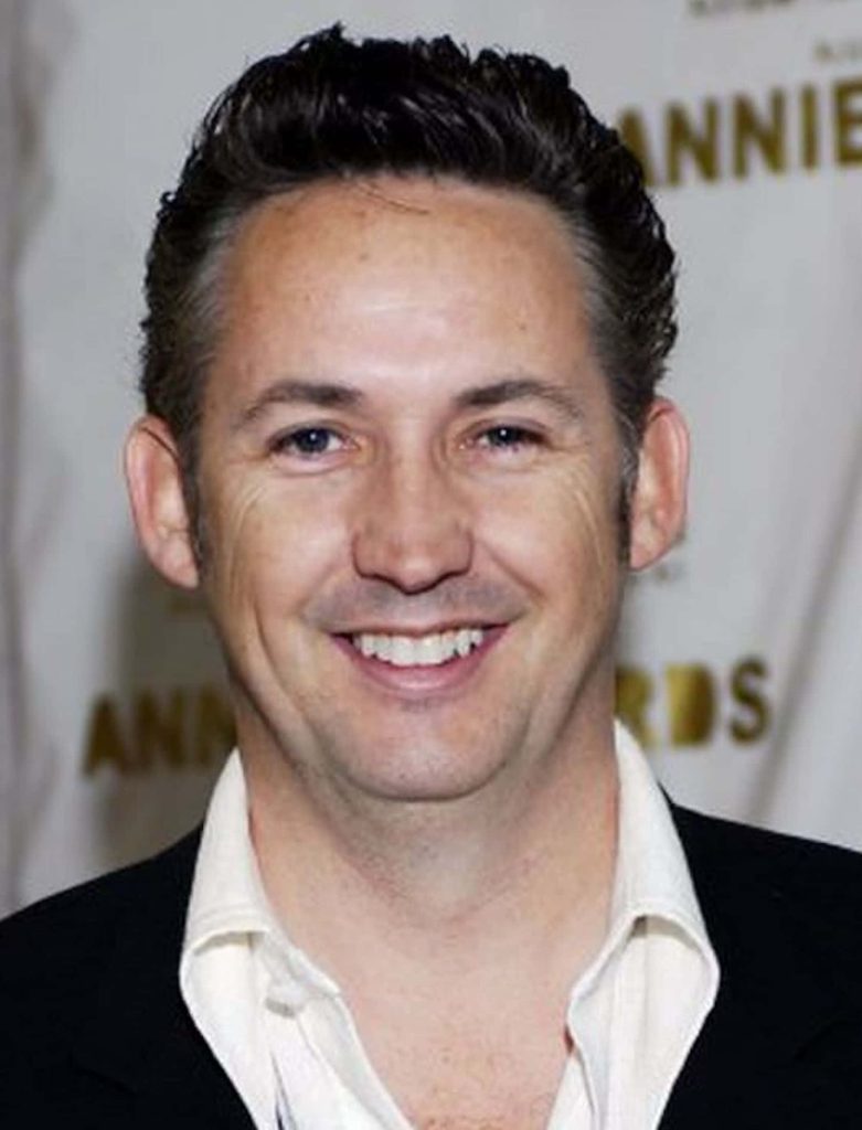 Harland Williams smiling in black blazer and white shirt at event with professional backdrop Wallpaper
