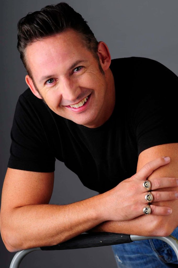 Harland Williams studio portrait smiling with rings black t-shirt grey background wallpaper